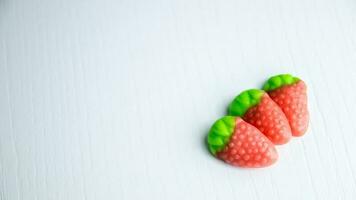 Three strawberries gummies on a white table with green leaf. photo