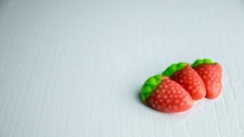 Three strawberries gummies on a white table with green leaf. photo