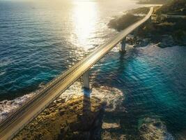 Aerial view of bridge, sea with waves and rocks at sunset photo