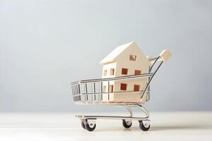A wooden house in a shopping cart on light gray background with copy space. Concept of buying real estate. . photo