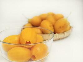 ripe juicy peeled marian plum or plum mango fruit serve in glass bowl and woven bamboo tray over white kitchen background, thailand fresh asian famous tropical fruit photo