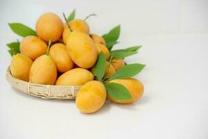 ripe juicy peeled marian plum or plum mango fruit serve in glass bowl and woven bamboo tray over white kitchen background, thailand fresh asian famous tropical fruit photo