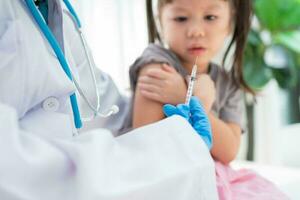 médico participación jeringuilla para preparar vacunado en el hombro de asiático niña niños en el hospital. pediatra hace vacunación para niños. vacunación, inmunización, enfermedad prevención concepto. foto