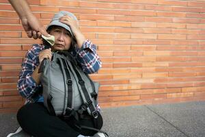 pobre cansado estresado Deprimido mayor asiático mujer Vagabundo sentado en el calle en el sombra de el edificio y mendicidad para ayuda y dinero, mayor asiático mujer abandonado concepto foto