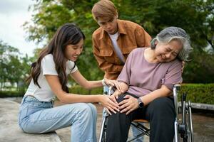 Asian careful caregiver or nurse taking care of the patient is hurting knee in wheelchair. Concept of happy retirement with care from caregiver and Savings and senior health insurance, a Happy family photo