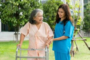 Asian careful caregiver or nurse hold patient hand and encourage patient, walking in garden. Concept of happy retirement with care from a caregiver and Savings and senior health insurance. photo