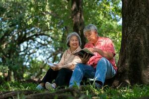 Happy Asian old senior couple with gray hair reading a book outside in park. Concept of happy elderly after retirement and good health photo