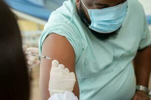 africano americano vestir un médico máscara y siendo codicioso vacunado para el prevención de coronavirus y gripe. concepto de inmunización desde inoculación foto