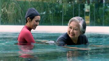 Young trainer helping senior woman in aqua aerobics and working out in the pool. old woman and mature man doing aqua aerobics exercise in swimming pool, Elderly sports, and active lifestyle concept. photo