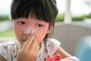 Adorable little child Asian girl paints her mouth with pink children heads and looks in the mirror. A child plays at home in a toy beauty salon. Increase learning development for preschoolers. photo