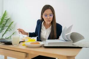 mujer de negocios ocupada y cansada comiendo espagueti para el almuerzo en la oficina y trabajando para entregar estados financieros a un jefe. con exceso de trabajo y poco saludable para comidas preparadas, concepto de agotamiento. foto