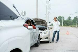 Asian men driver check for damage after a car accident before taking pictures and sending insurance. Online car accident insurance claim after submitting photos and evidence to an insurance company.