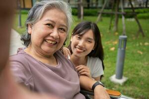 Happy Asian patients in a wheelchair use smartphones to take pictures with careful caregivers or nurse Concept of happy retirement with care from a caregiver and Savings and senior health insurance. photo
