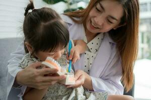 Asian female dentist teaching cute little girl brushing teeth with toothbrush and stomatologist telling girl child about oral hygiene in dental clinic, Education and prevention cavities concept. photo