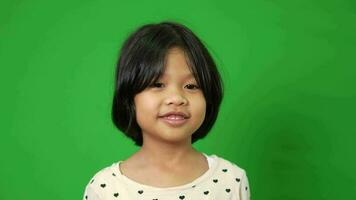Porträt von Glücklich, lächelnd, und komisch asiatisch Kind Mädchen auf Grün Bildschirm Hintergrund, ein Kind suchen beim Kamera. Vorschule Kind träumend füllen mit Energie Gefühl gesund und gut Konzept video