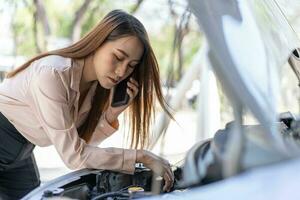 enojado asiático mujer utilizando un teléfono inteligente vídeo conferencia para asistencia después un coche Descompostura en calle. concepto de un vehículo motor problema o accidente y emergencia ayuda desde un profesional mecánico foto