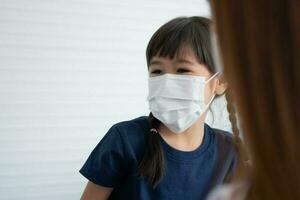 Asian parents wear face masks to little daughter for protection against coronavirus covid 19 before going to school. Mom teaches daughter to put on a medical mask photo