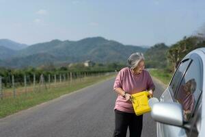 The car ran out of gas and stalled beside the road in suburbs and an elderly Asian woman used a gallon of spare gas to fuel the car. A woman prepares a gallon of spare gas to fuel before traveling. photo