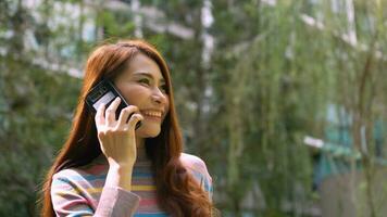 A smiling female tourist talking via smartphone on the park in the hotel. Feel happy. Close up happy woman chatting on mobile phone outdoor. photo