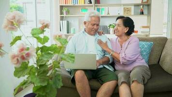 contento asiatico coppia seduta su divano e utilizzando un' il computer portatile per Surf il Internet e video conferenza con famiglia. concetto di tecnologia portando famiglie più vicino, sociale distanziamento