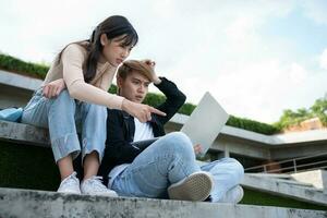 Asian students sitting on steps and use computer laptops to discuss before exams, Student lifestyle at university. Group of student do a project together photo