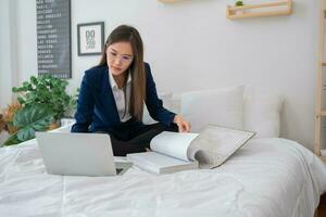 Overworked and Stressed young Asian woman working on laptop computer and document paper in bed at hotel, Business trip, Burnout, technology, copy space, Professional Burnout And Exhaustion Concept. photo