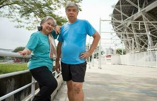 contento y sonrisa parejas mayor asiático en pie en escalera para descanso después ejercicio, trotar en mañana, mayor ejercicio al aire libre para bueno saludable. concepto de cuidado de la salud y activo estilo de vida para sano foto