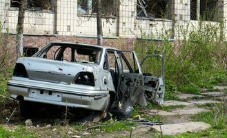 A broken car, shot by artillery, stands in the courtyard of a multi-storey residential building. War between Russia and Ukraine. The wreckage of an abandoned car. photo