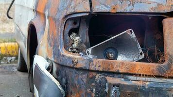 Burnt car body. Arson, short circuit. The skeleton of a burnt car. Front view of a burnt and abandoned rusty van and a broken headlight. photo