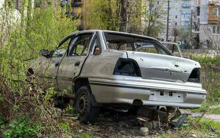 un roto ucranio civil auto, Disparo por artillería, soportes en el patio de un destruido casa. guerra Entre Rusia y Ucrania. el destrucción de un abandonado coche. foto