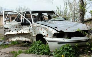 The car that burned down after the bombing of the city stands in the courtyard of a destroyed house. War between Russia and Ukraine. Fragments of a car after artillery shelling. photo