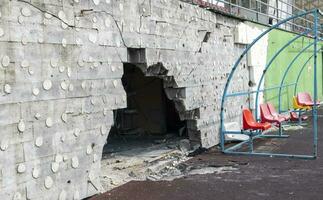 guerra en Ucrania. roto el plastico bancos para aficionados en el podio, en un destruido fútbol americano estadio en un para niños fútbol americano escuela. el Consecuencias de bombardeo desde artillería. foto