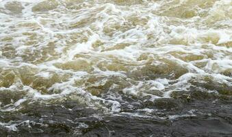 River rapids. Close up abstract background of falling water. Water flows over river rocks. A beautiful powerful stream of a stormy mountain river. The river rushes with fast-flowing water. photo