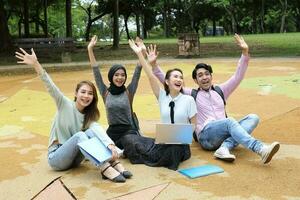 Young asian malay chinese man woman outdoor park sit on ground study talk discuss point laptop file book backpack mingle fun wave hello greet photo