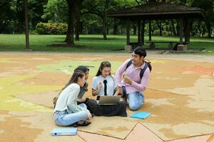 joven asiático malayo chino hombre mujer al aire libre parque libro archivo carpeta ordenador portátil computadora teléfono sentar estar estudiar mezclarse foto