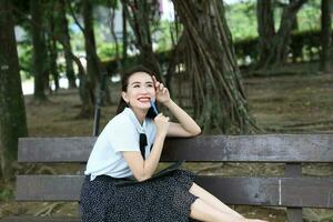 Young asian chinese woman outdoor on park bench hold file book folder read write see smile look pen in hand photo