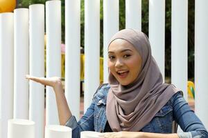 Young Asian Malay muslim woman headscarf outdoor green pose show display palm of hand photo