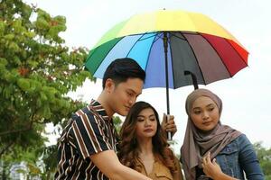 Young Asian Malay man woman outdoor green park walk talk discuss mingle under umbrella photo