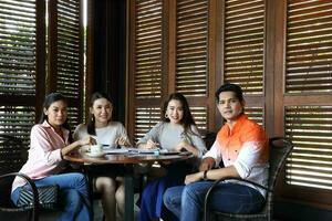 Group young asian malay man woman at rustic wooden cafe table meet talk discuss look front at camera photo