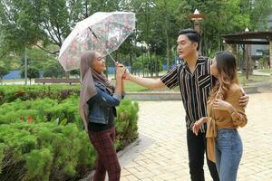 Young Asian Malay man woman outdoor green park walk talk discuss mingle under umbrella photo