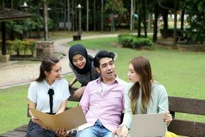 joven asiático malayo chino hombre mujer al aire libre parque libro archivo carpeta ordenador portátil computadora teléfono sentar estar estudiar mezclarse foto