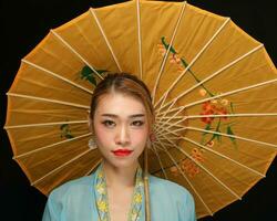 Asian woman in tractional kebaya behind umbrella on black background photo