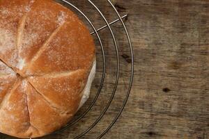 Freshly baked bread loaf round on metal grill over rustic wood background photo