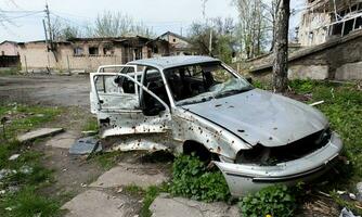 A broken Ukrainian civilian car, shot by artillery, stands in the courtyard of a destroyed house. War between Russia and Ukraine. The wreckage of an abandoned car. photo