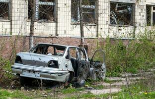 The car that burned down after the bombing of the city stands in the courtyard of a destroyed house. War between Russia and Ukraine. Fragments of a car after artillery shelling. photo