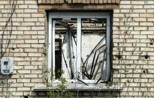 The buildings were hit by shelling. One window and damaged brick facade of architecture. Houses after fighting in the city. Destroyed houses in the city during the war in Ukraine. photo