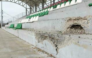 guerra en Ucrania. roto el plastico bancos para aficionados en el podio, en un destruido fútbol americano estadio en un para niños fútbol americano escuela. el Consecuencias de bombardeo desde artillería. foto