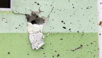 agujeros desde balas y metralla en el pared en el frente línea. cicatrices de guerra. hormigón pared de un residencial edificio con baches y agujeros desde tiroteo. Consecuencias de el guerra en Ucrania. foto