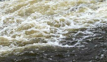 River rapids. Close up abstract background of falling water. Water flows over river rocks. A beautiful powerful stream of a stormy mountain river. The river rushes with fast-flowing water. photo