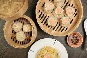 Prawn shrimp shaomai Xiao long bao dim sum dumpling chicken prawn fish seafood vegetable in bamboo steamer fried rice on plate sauce chopsticks soup spoon over rustic background photo